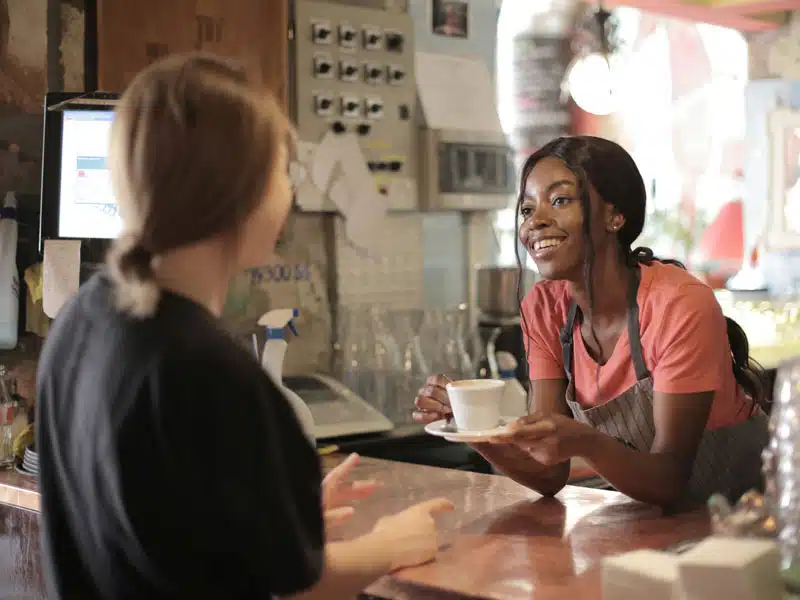 A lady holding a cup of coffee talking to a customer